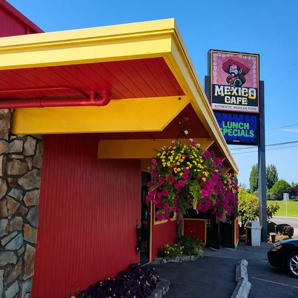 Exterior of Mexico Cafe, a red building with yellow trim, hanging flowers, and a sign.