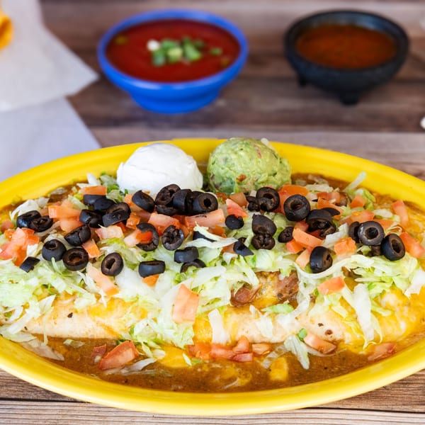 A large burrito covered in lettuce, tomatoes, black olives, sour cream, and guacamole.