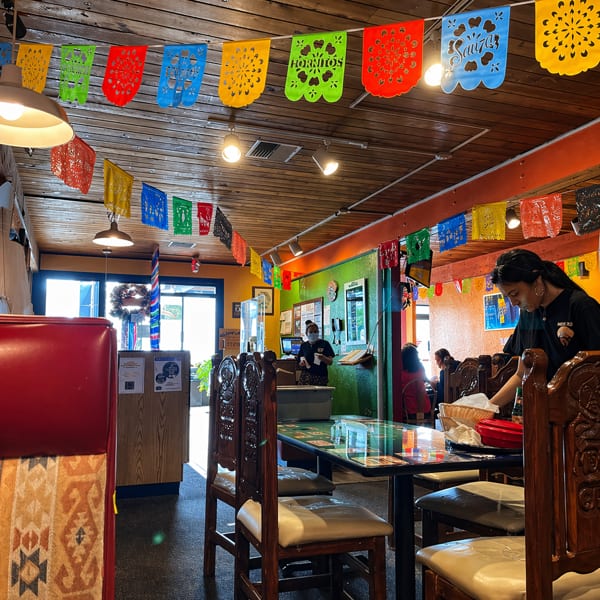 A vibrant Mexican restaurant interior with colorful papel picado banners, wooden tables, and a server.