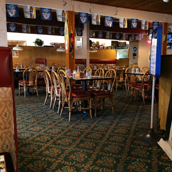 Empty restaurant dining room with wooden tables, red chairs, and beer banners hanging from the ceiling.