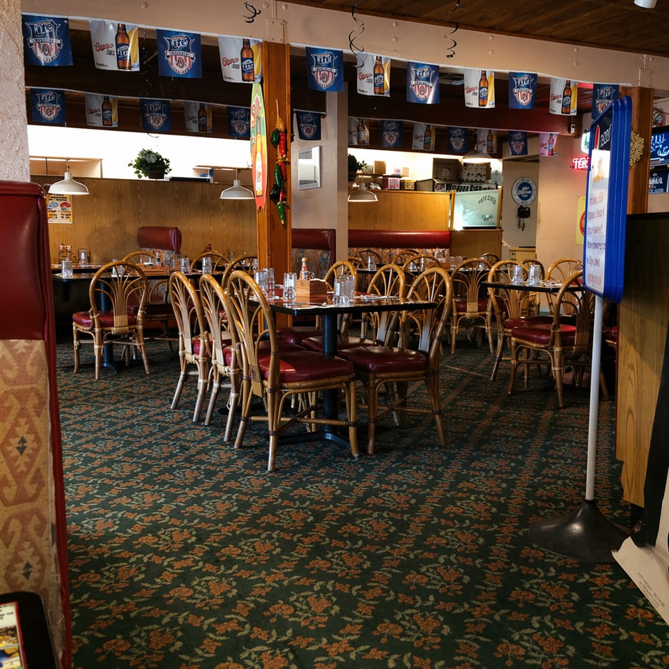 Empty restaurant dining room with wooden tables, red chairs, and beer banners hanging from the ceiling.