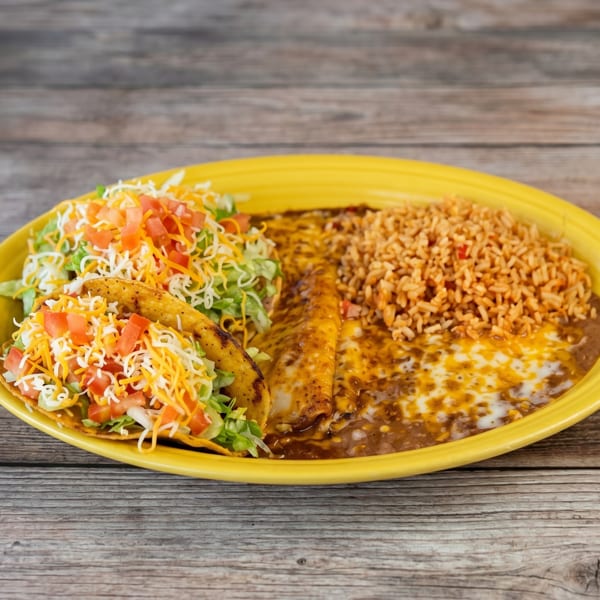 A yellow plate holds two tacos, enchiladas, refried beans, and rice on a wooden table.
