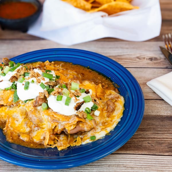 A blue plate of cheesy enchiladas topped with sour cream, green onions, and crispy fried onions.