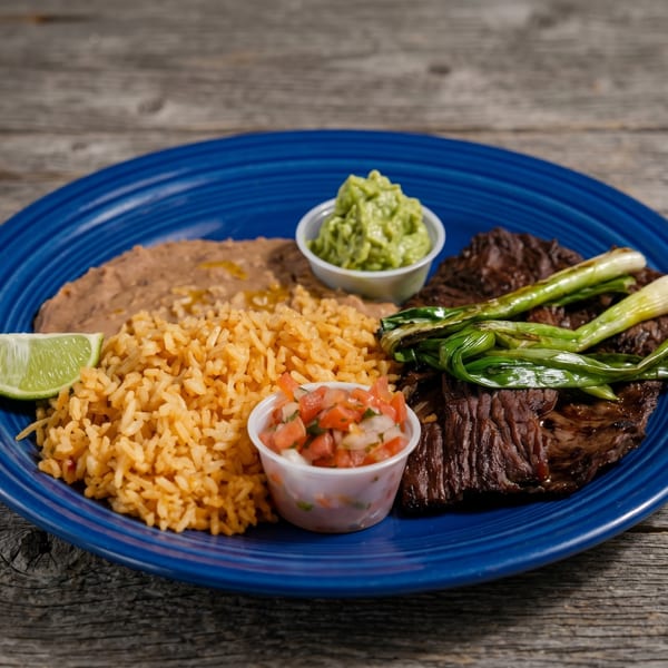 Carne asada with grilled green onions, rice, refried beans, guacamole, pico de gallo, and a lime wedge.